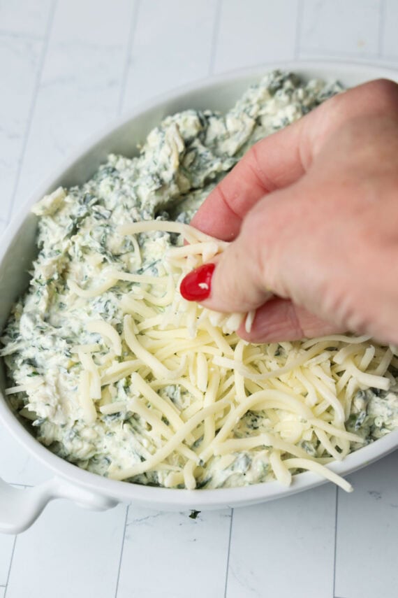 Topping spinach and artichoke dip with grated mozzarella cheese before baking.