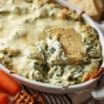 A tortilla chip scooping out spinach and artichoke dip