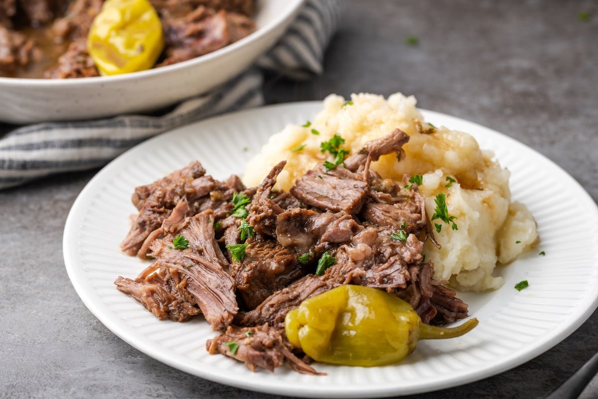 Mississippi pot roast on a white plate next to mashed potatoes.