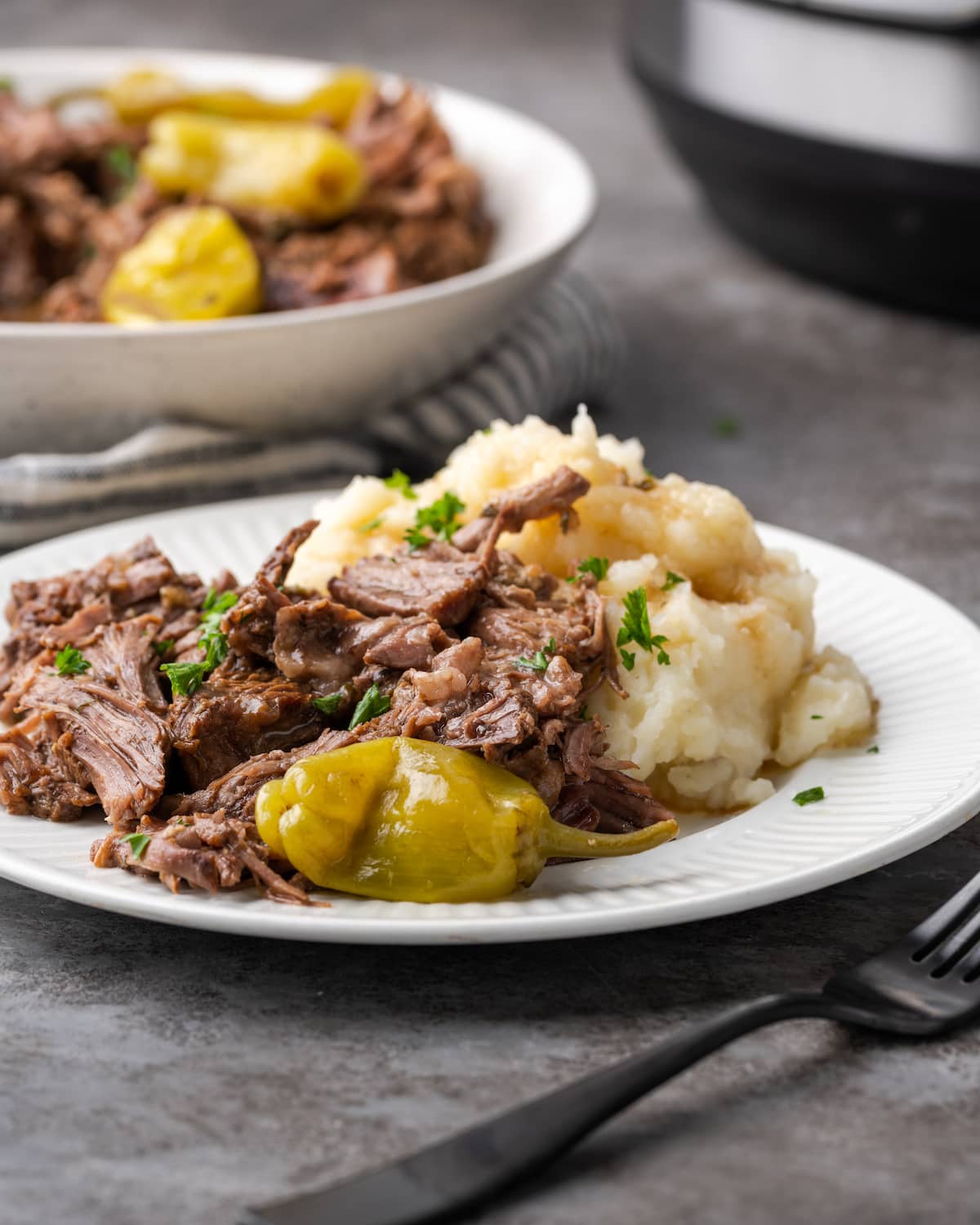 Mississippi pot roast on a white plate next to mashed potatoes.