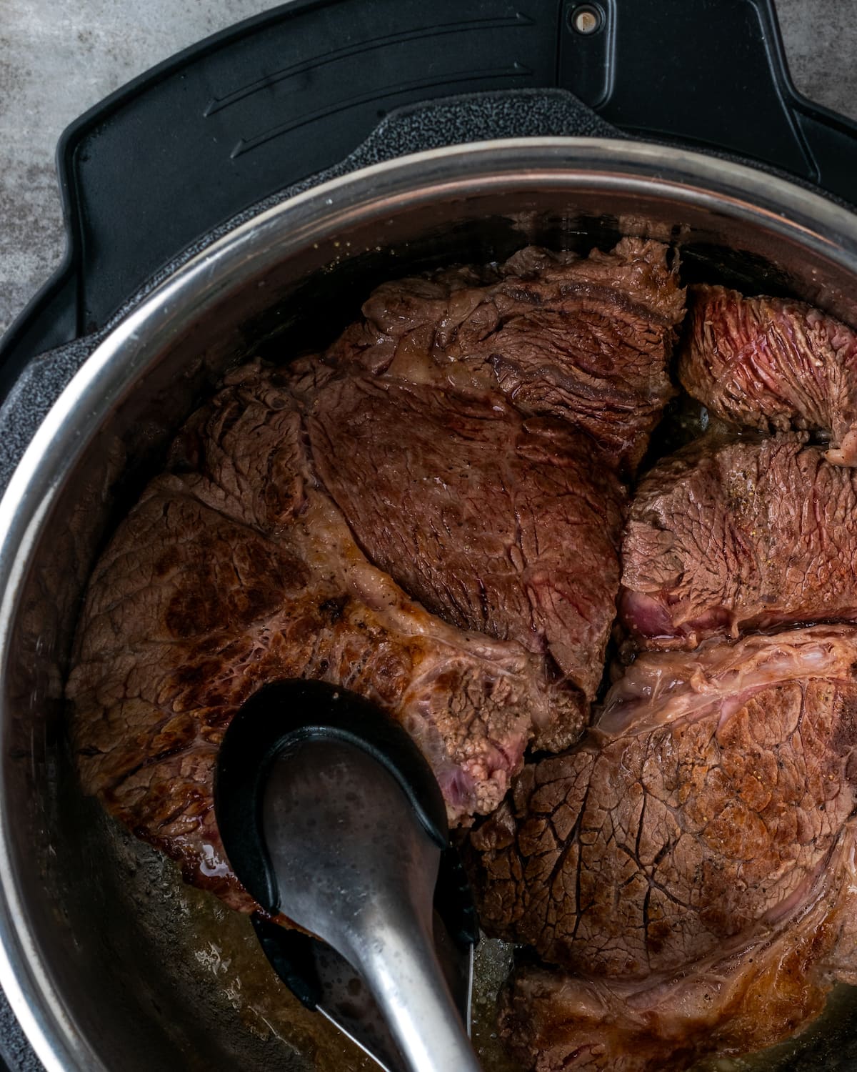 Tongs are used to move around seared chuck roast inside the Instant Pot.