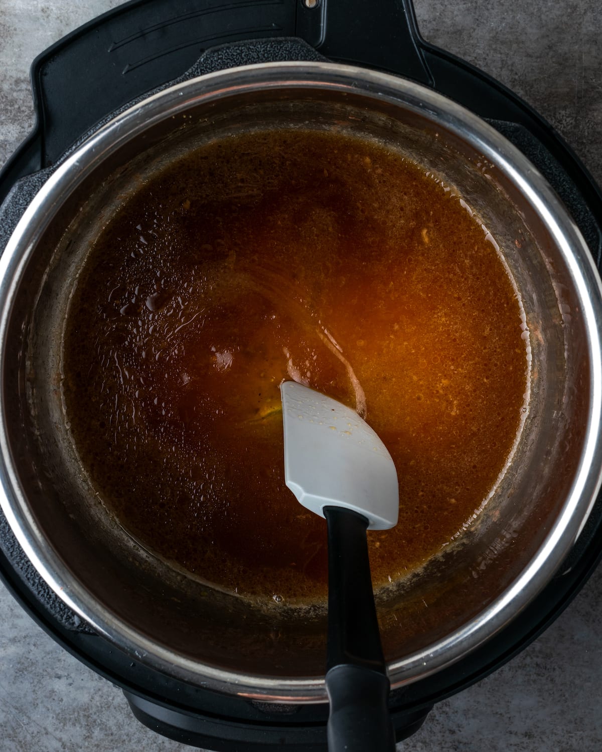 A spatula is used to stir beef broth in the bottom of the Instant Pot.