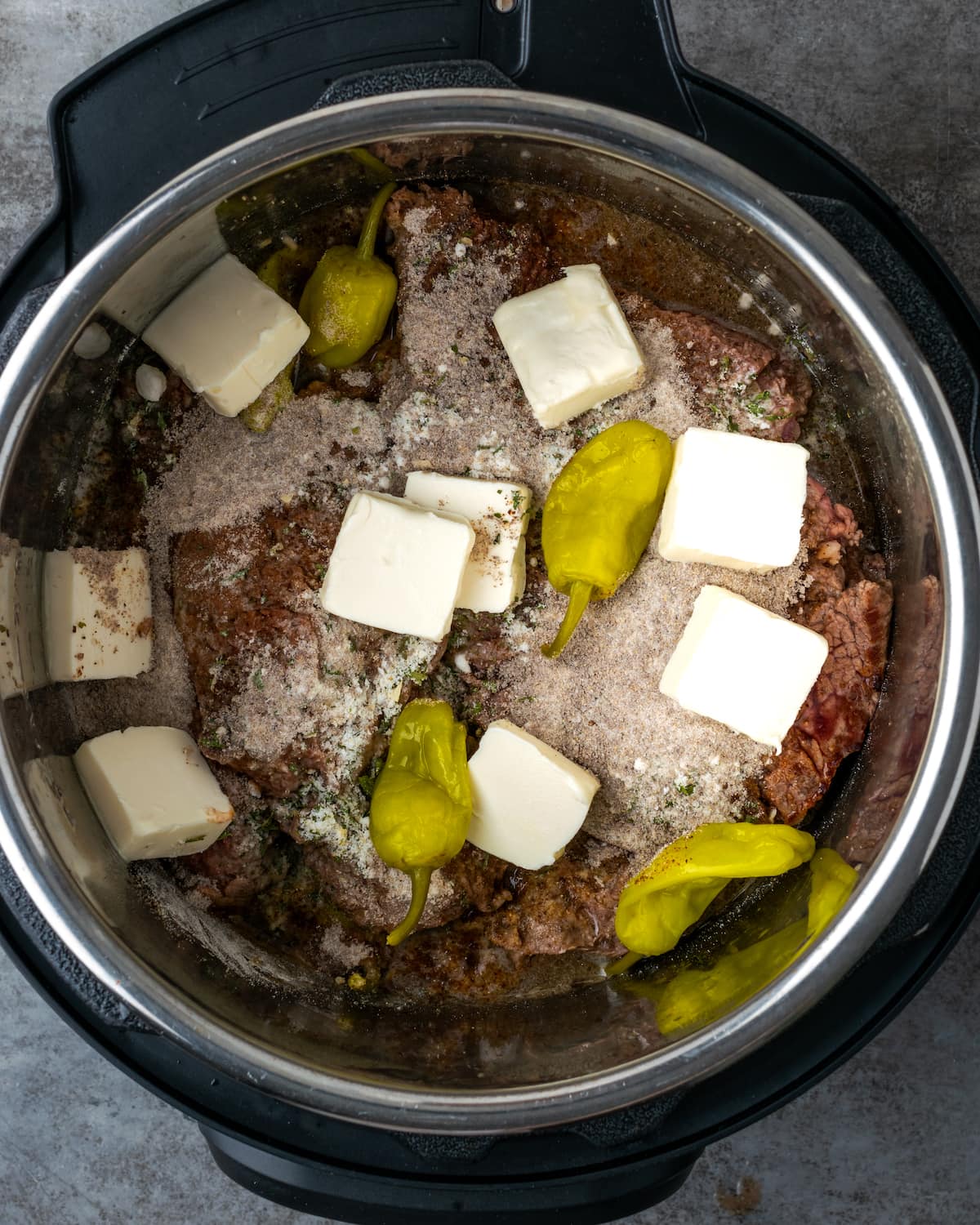 Seasoning, gravy mix, pepperoncini and pats of butter are added over top of the beef inside the Instant Pot.