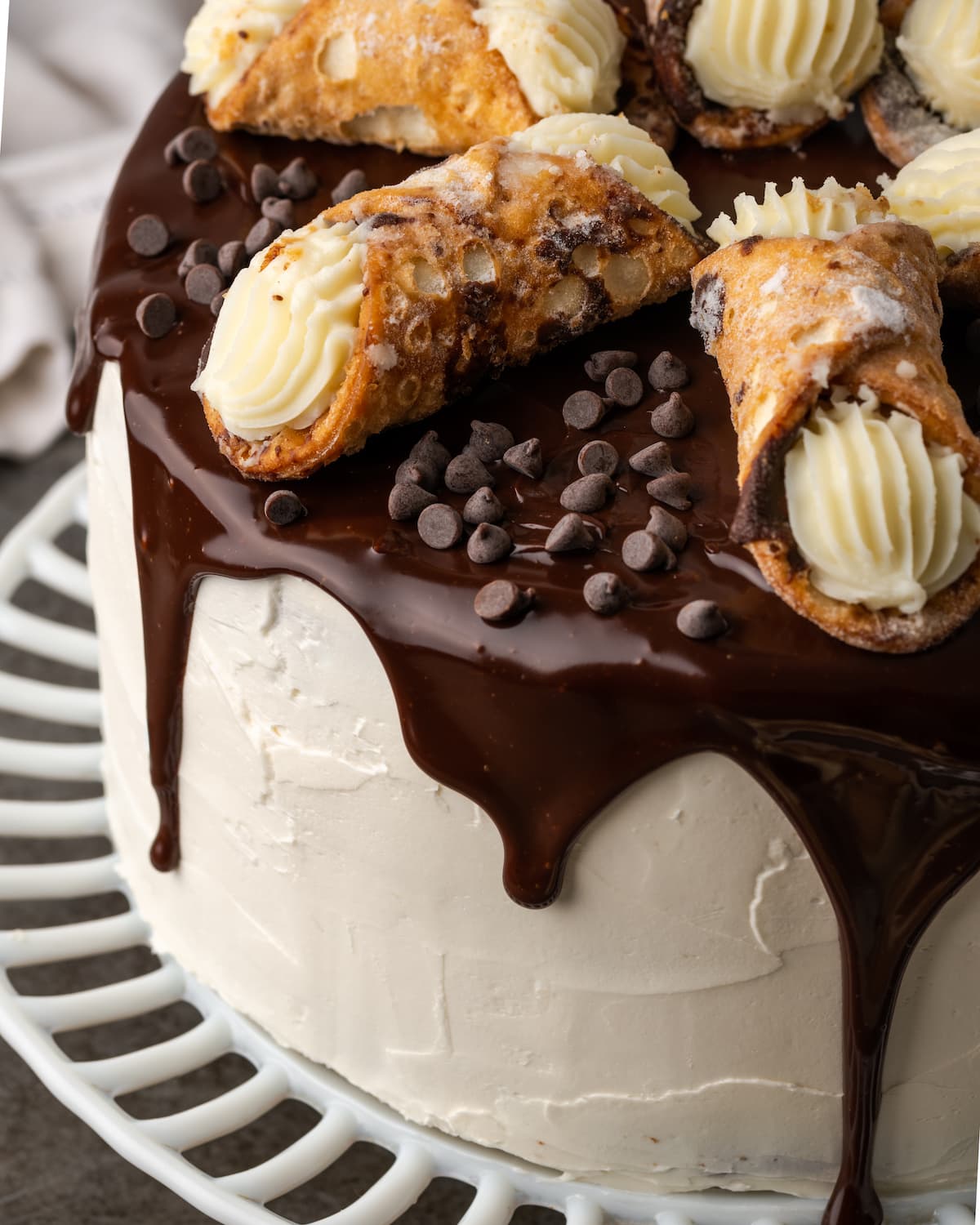 Top view of cannoli cake on a cake stand drizzled with chocolate ganache and garnished with cannoli pastries.
