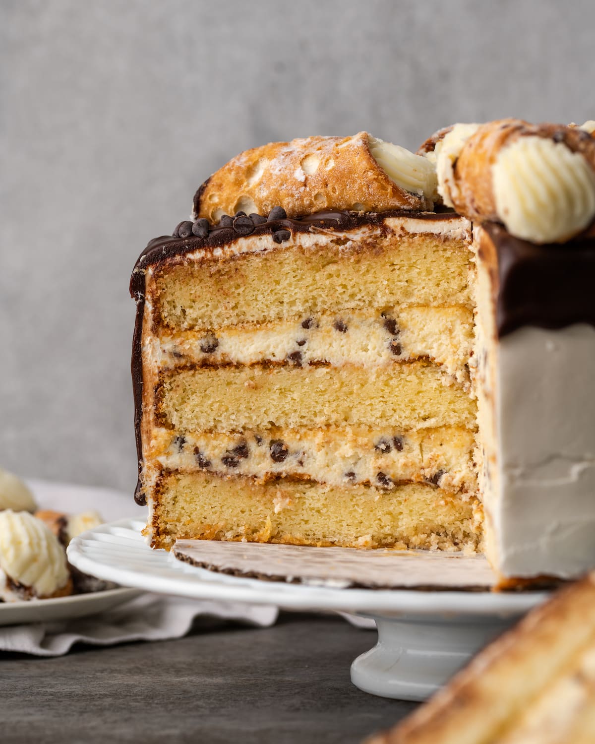 A finished cannoli cake with slices missing to reveal the layers of vanilla cake and cream filling.