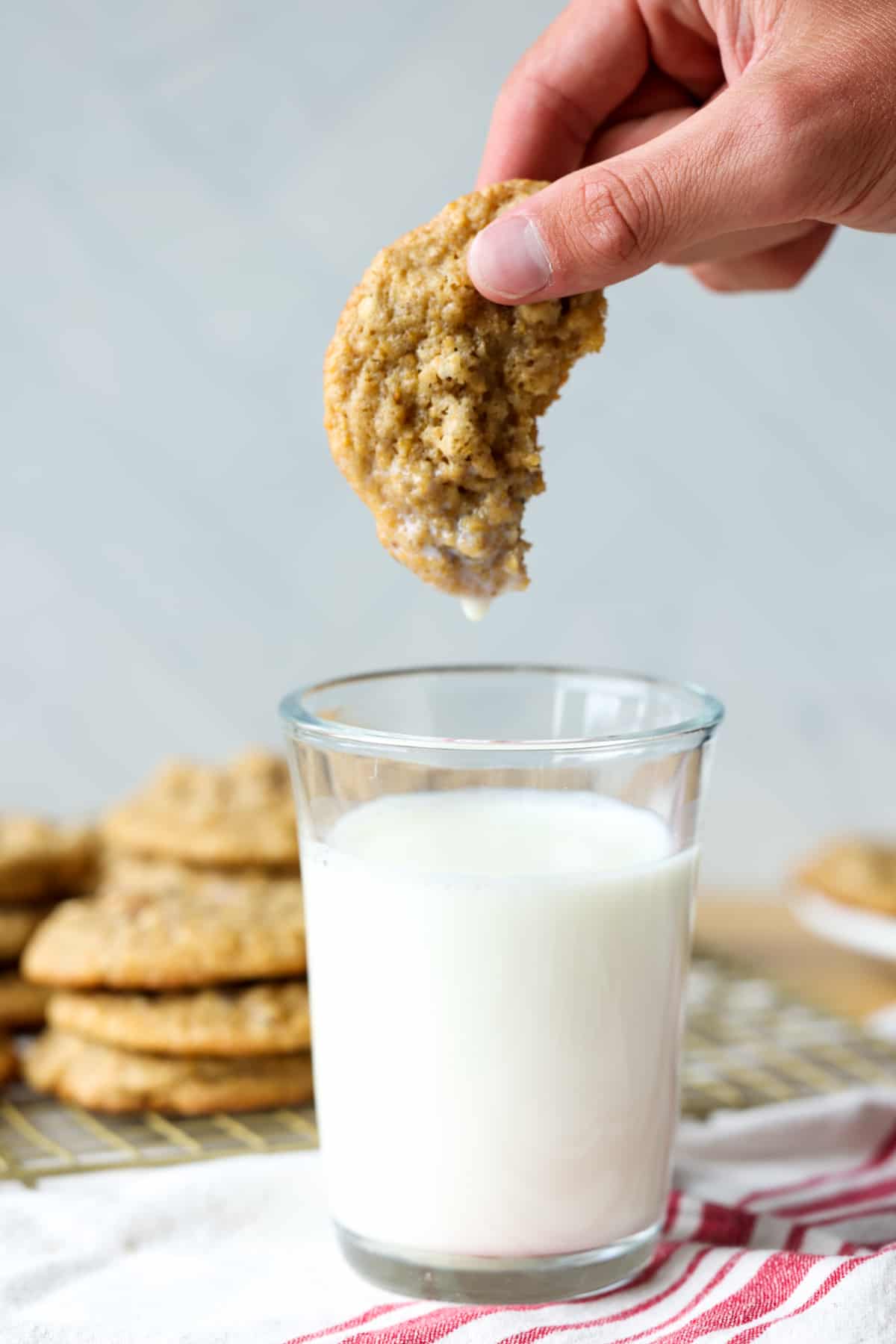 Dunked pecan cookie in a clear glass of milk with milk dripping off the cookie