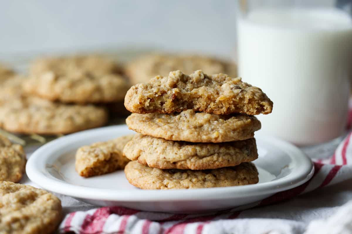 Stacked pecan cookies on a white plate with a glass of milk in the background.