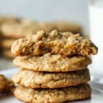 A stack of four pecan cookies with the top one broken in half and a glass of milk in the background.