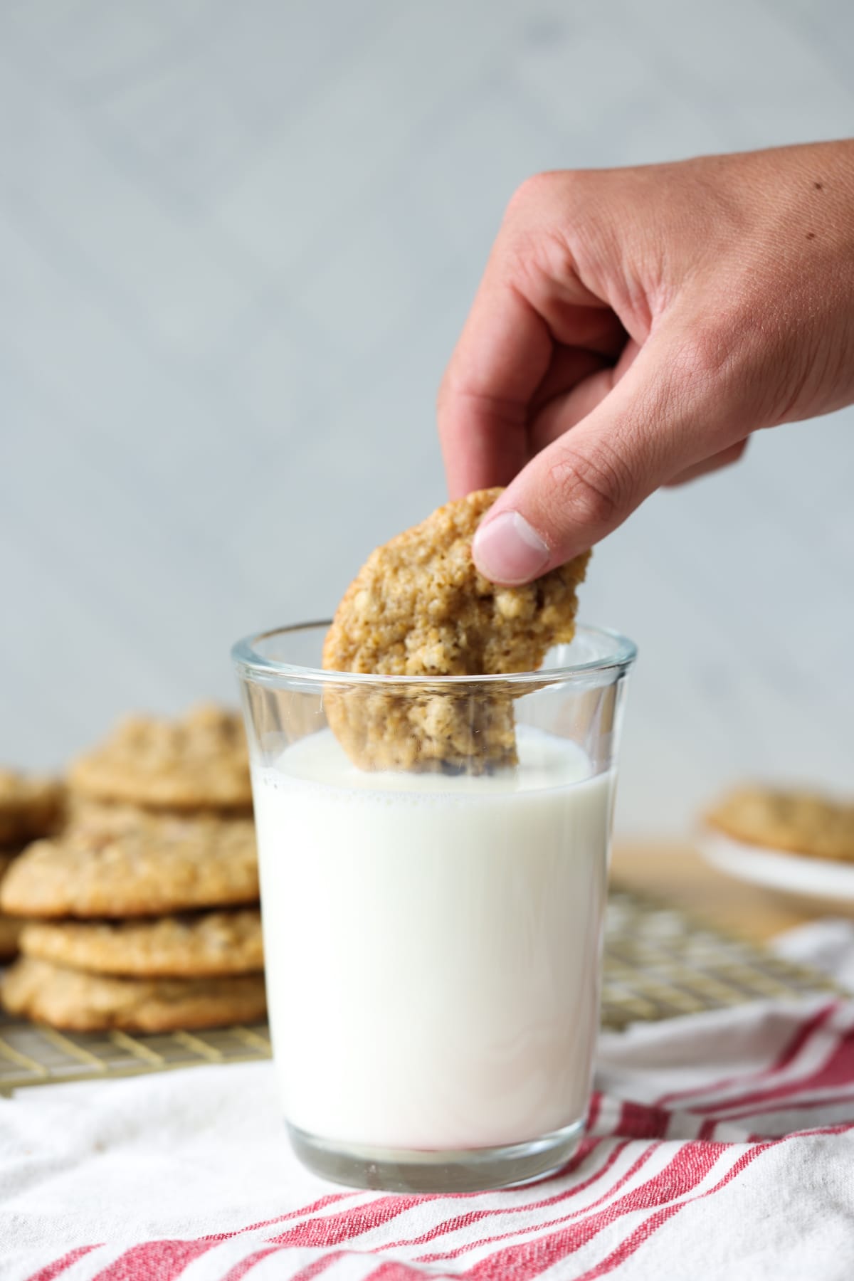 A hand dunking half a pecan cookie in a clear glass of milk