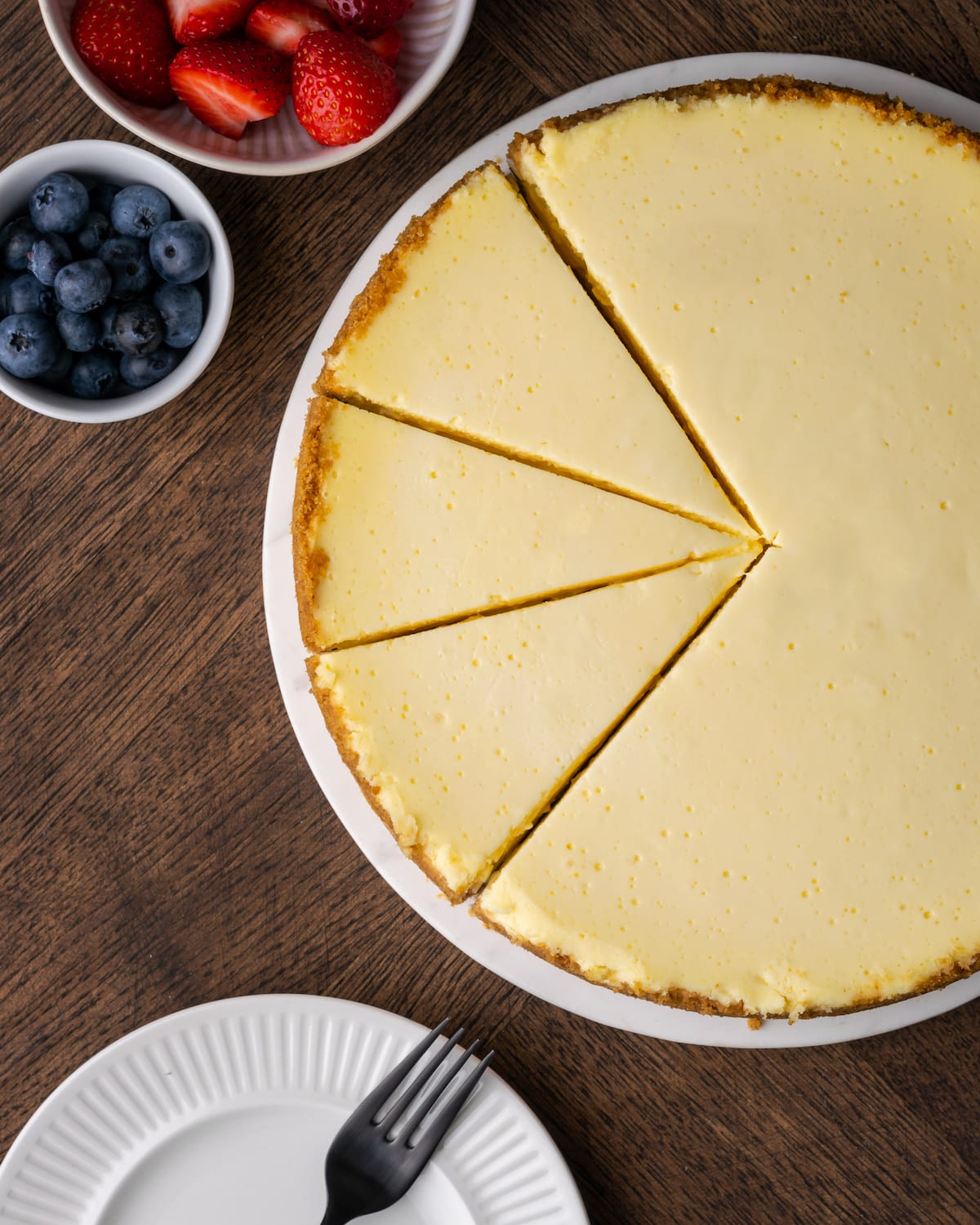 Overhead view of a sour cream cheesecake with three slices cut into it.