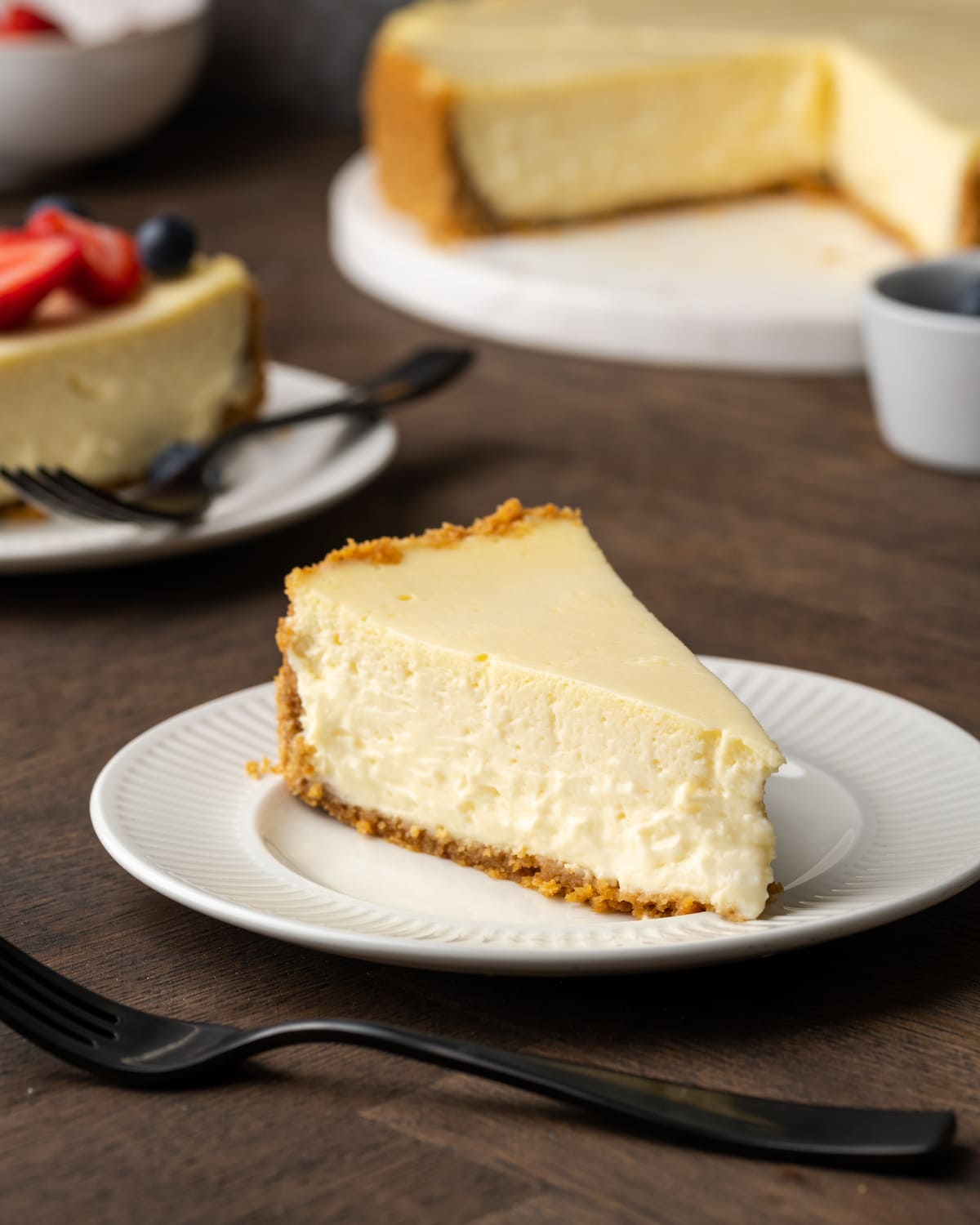 A slice of sour cream cheesecake on a white plate.