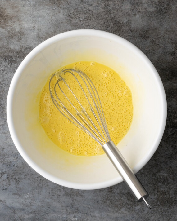 The egg mixture for cheesecake batter in a large mixing bowl with a whisk.