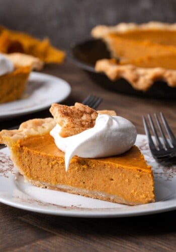 A slice of pumpkin pie on a plate topped with whipped cream and a sugar cookie, next to a fork.