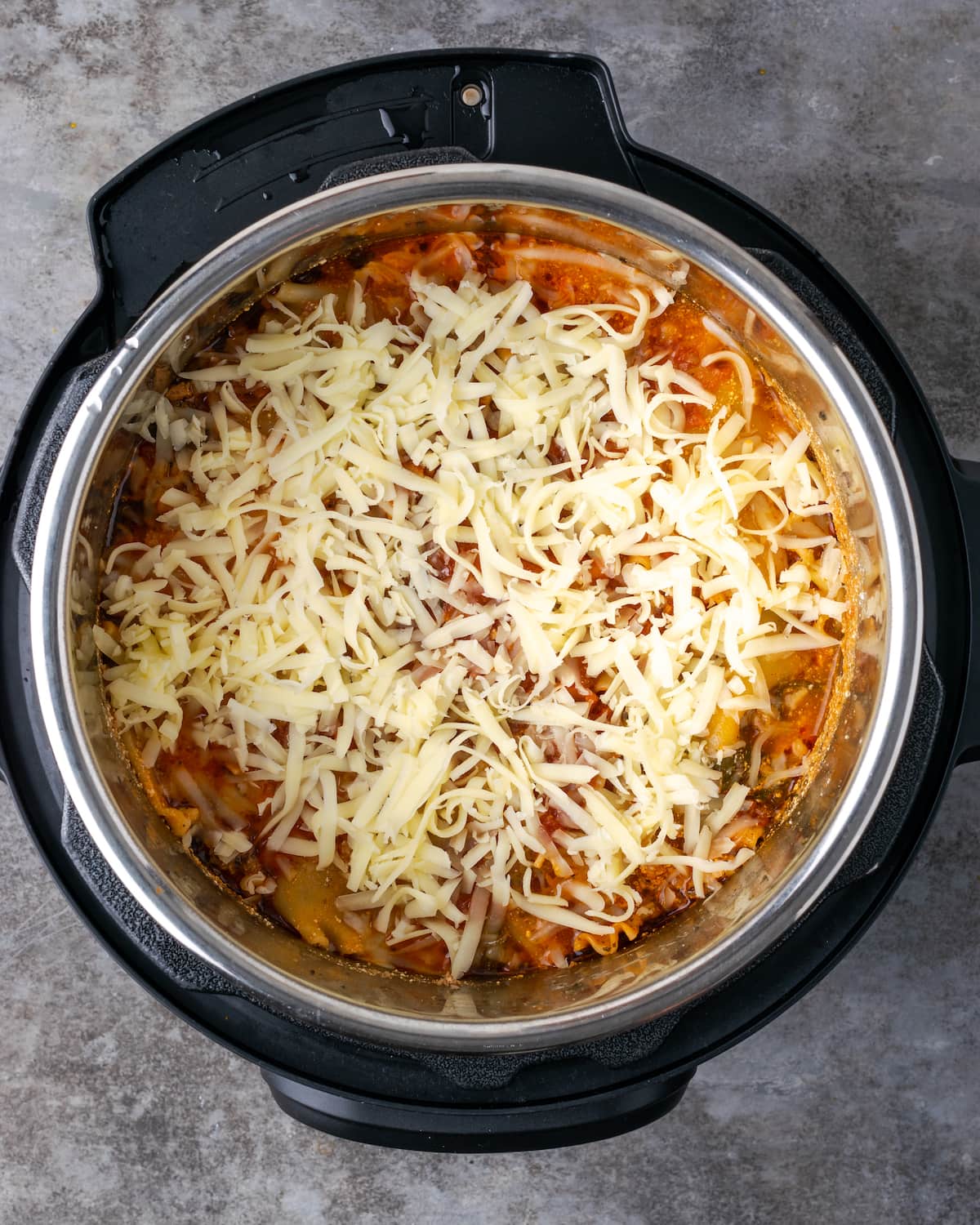 Overhead view of cooked Instant Pot lasagna topped with shredded mozzarella inside the pot.