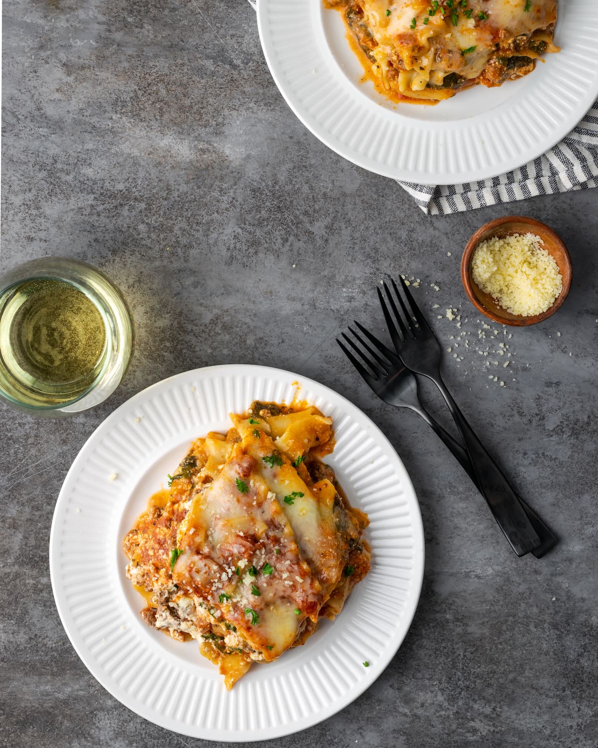 Overhead view of two servings of Instant Pot lasagna on plates next to a glass of wine and two forks.