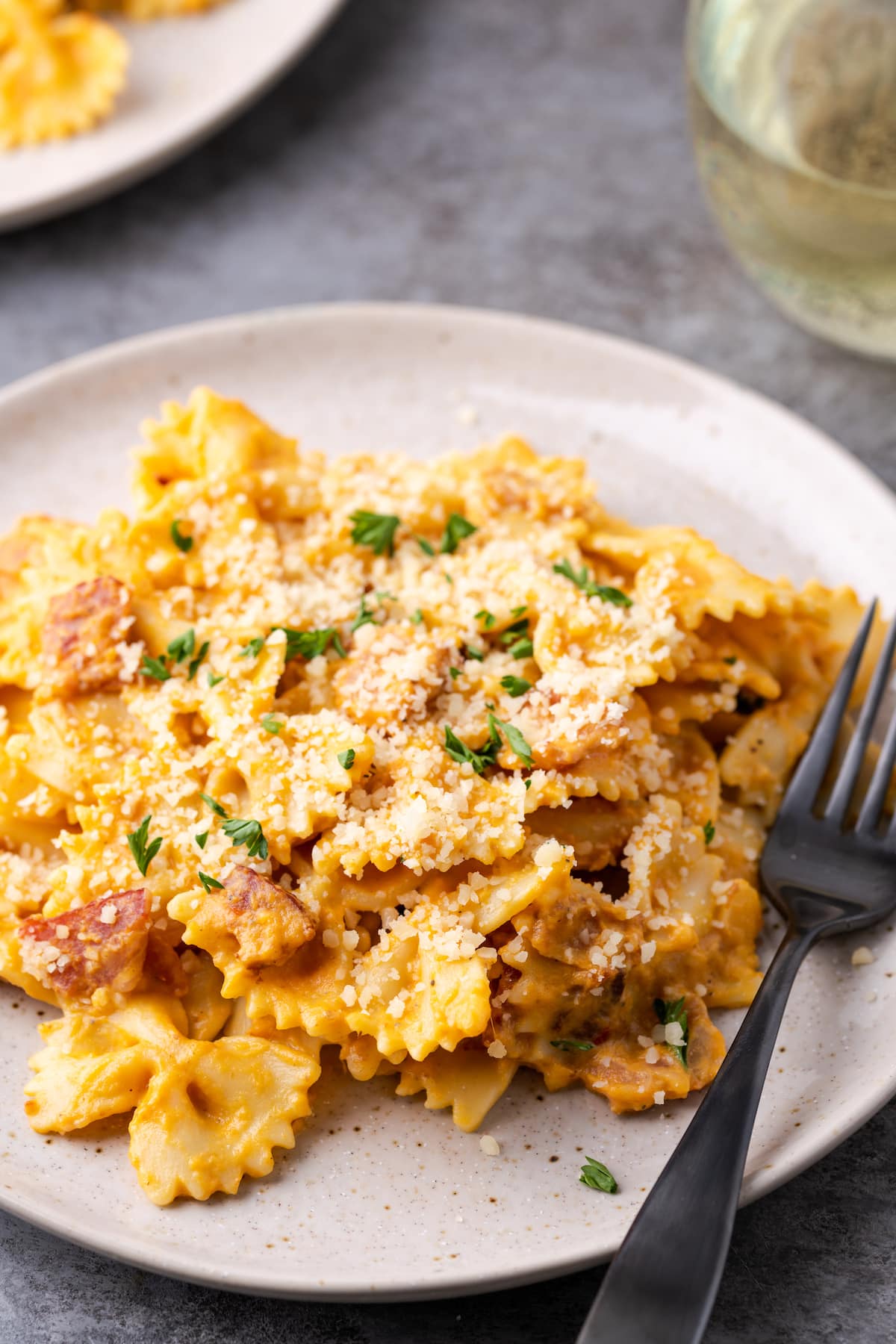 A serving of pumpkin pasta with bacon on a plate next to a fork.