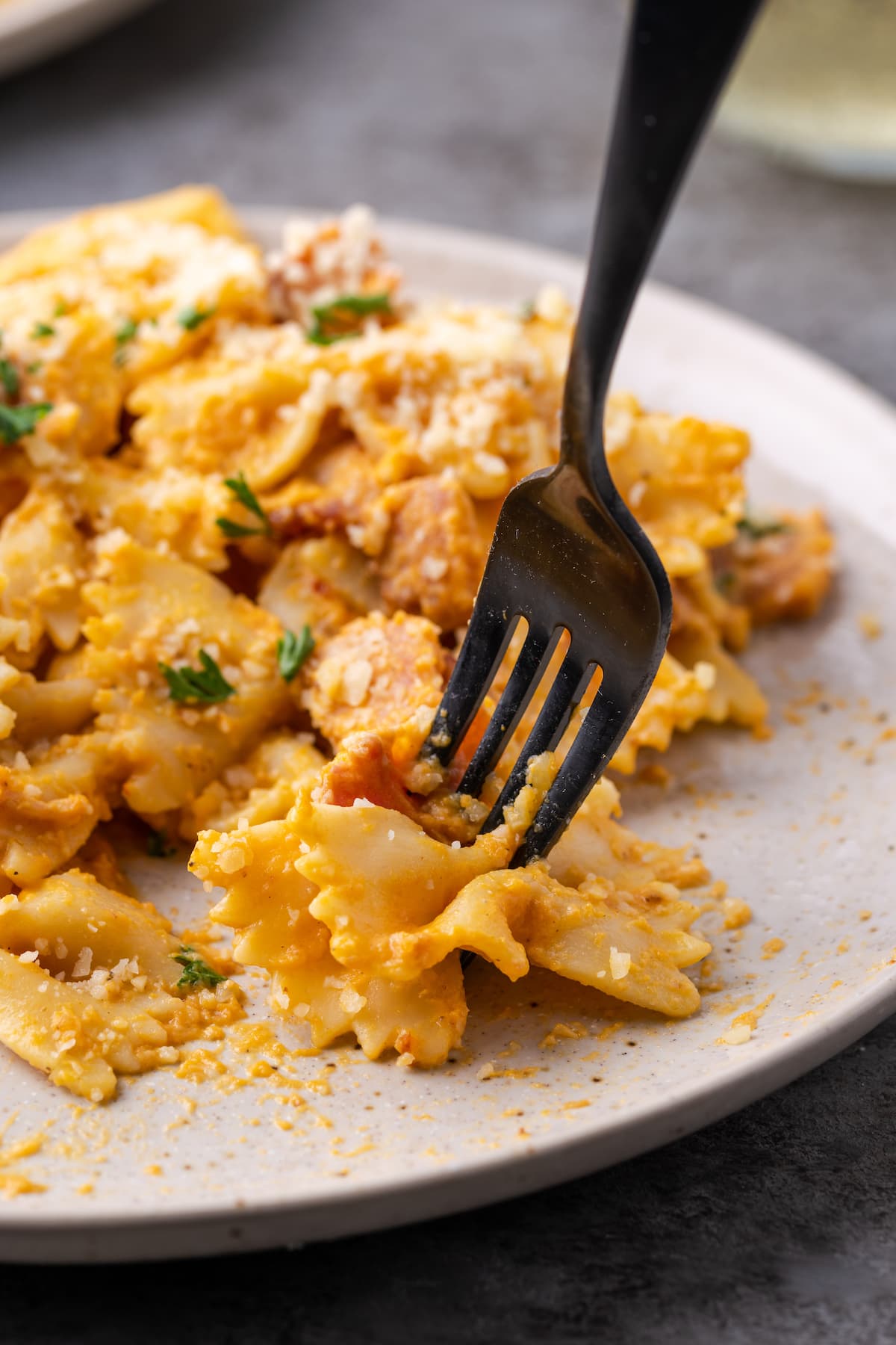 A fork picks up a bite of farfalle pumpkin pasta with bacon from a plate.