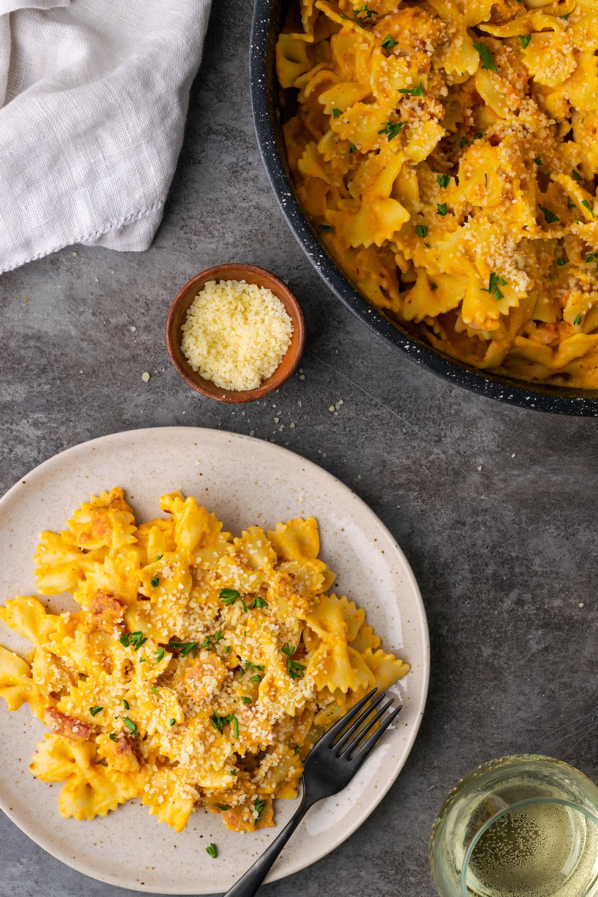 A plate of pumpkin pasta with bacon next to a black serving bowl full of pumpkin pasta.