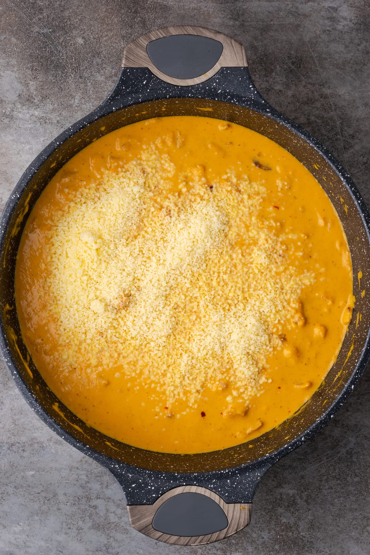 Parmesan cheese is added to the pumpkin cream sauce in a cast iron skillet.