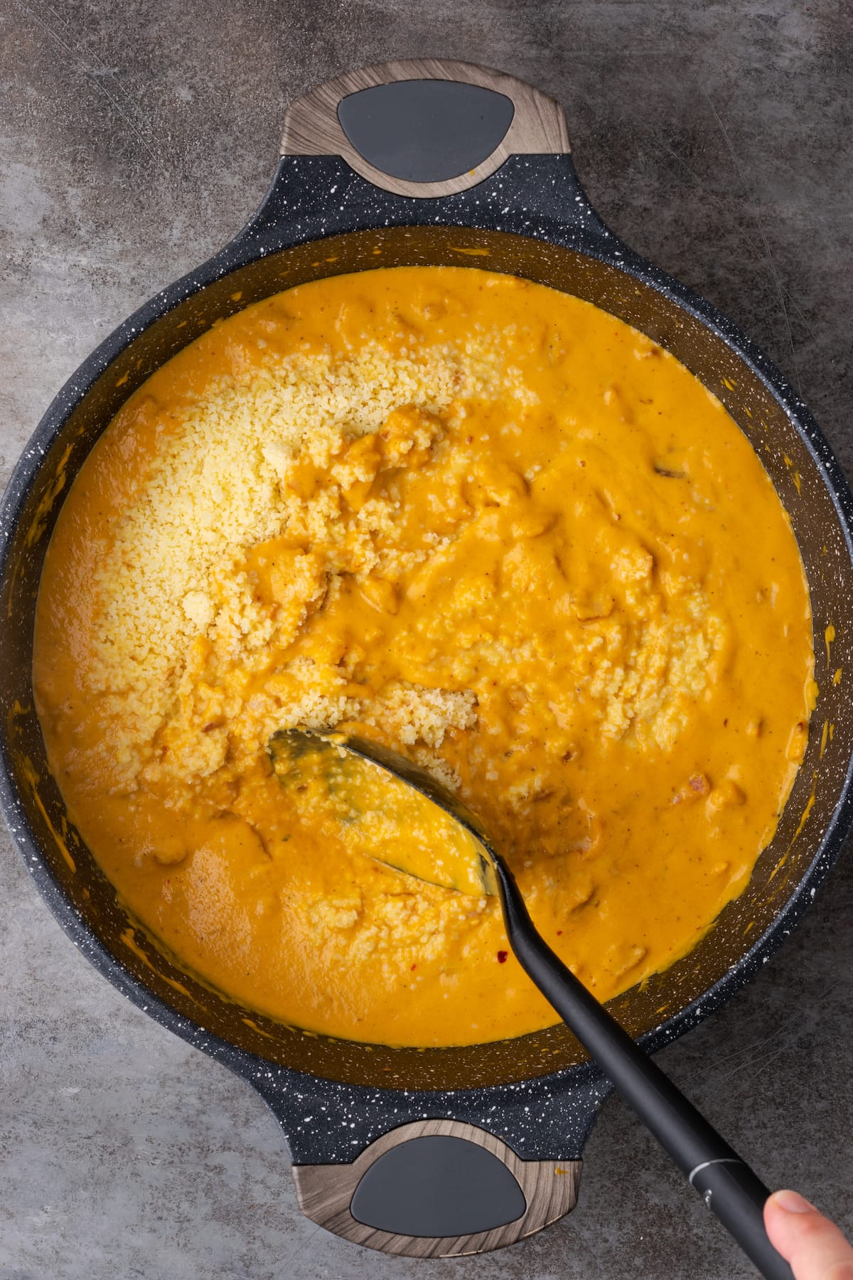 Cooked farfalle pasta is stirred into pumpkin cream sauce with bacon in a cast iron skillet.