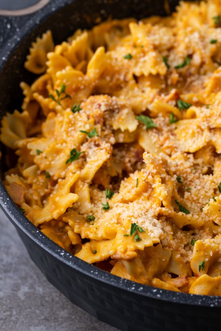 Creamy pumpkin pasta with bacon in a large black serving bowl.
