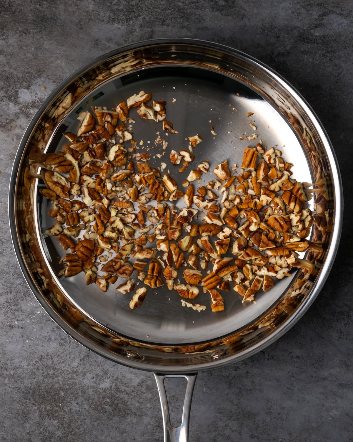 Pecans toasting in a large metal skillet.