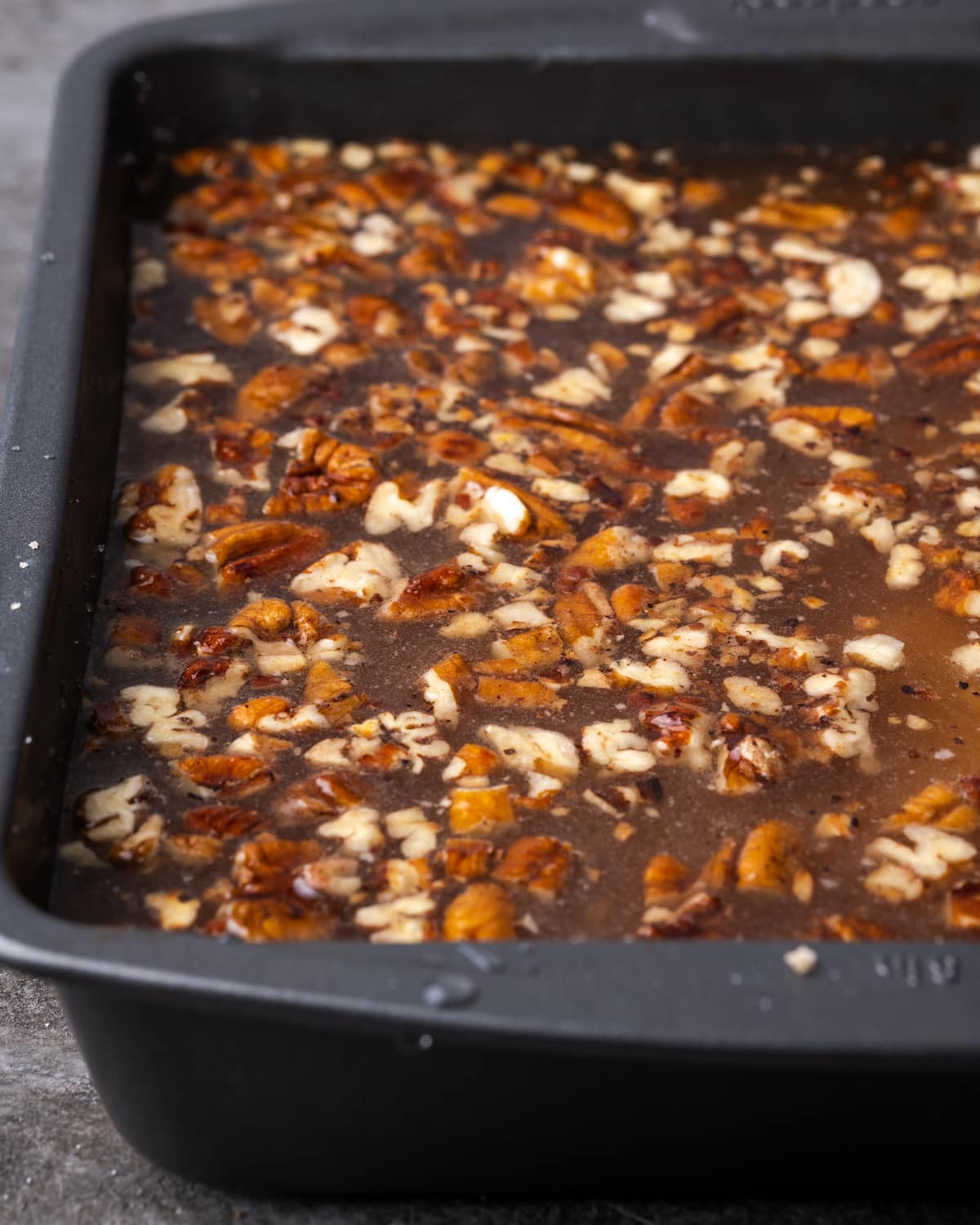 Pumpkin cobbler in a baking pan topped with toasted pecans, brown sugar, and hot water before baking.