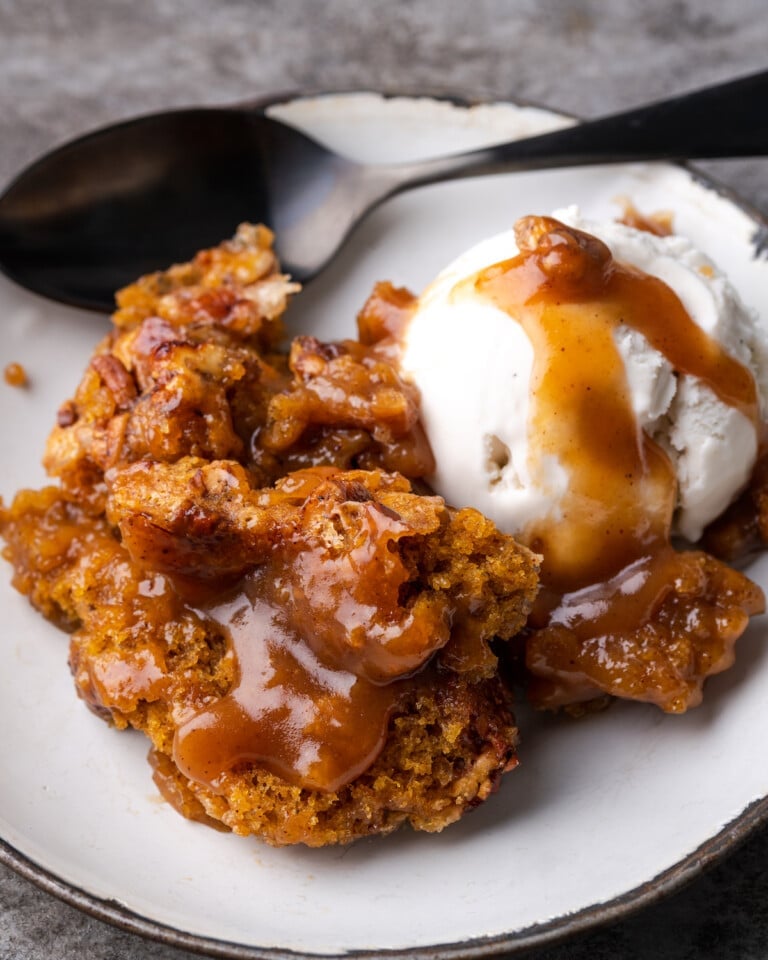 Pumpkin cobbler on a white plate topped with vanilla ice cream and caramel sauce.