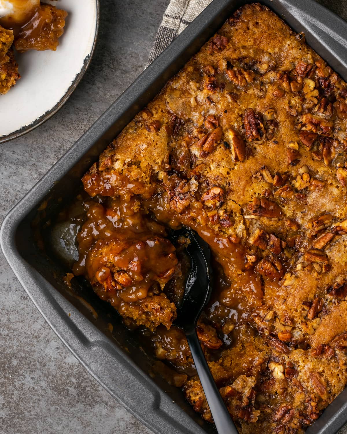 Overhead view of pumpkin cobbler in a baking pan, with a serving scooped out onto a plate.