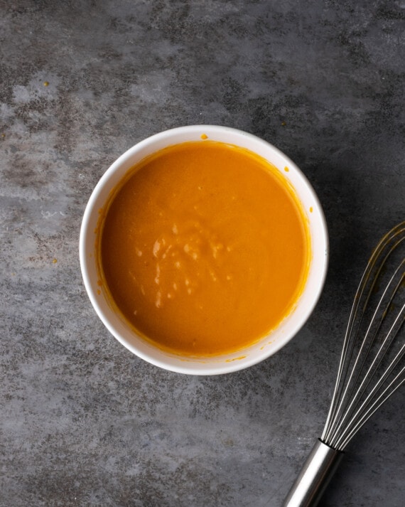 The wet ingredients for the pumpkin cobbler batter combined in a white bowl.