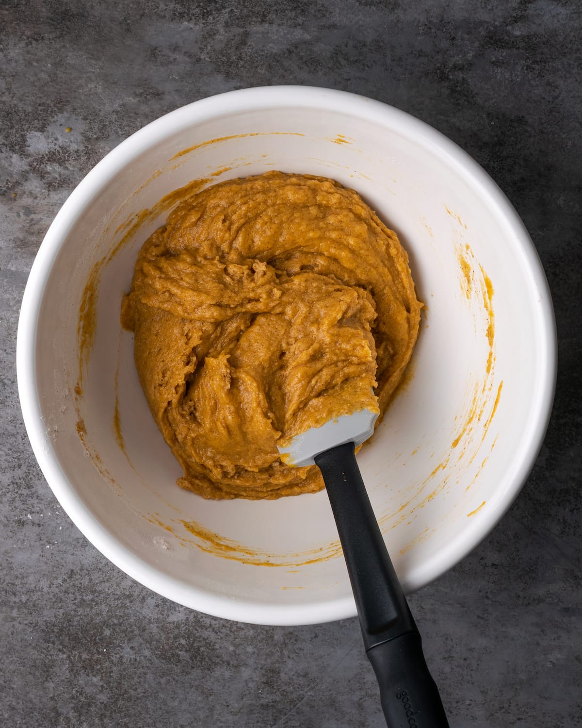 Pumpkin cake batter in the bottom of a mixing bowl with a spatula.