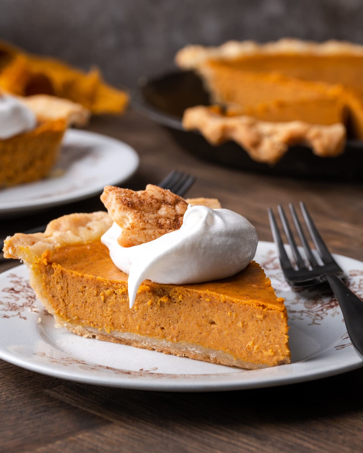 A slice of pumpkin pie on a plate topped with whipped cream and a sugar cookie, next to a fork.