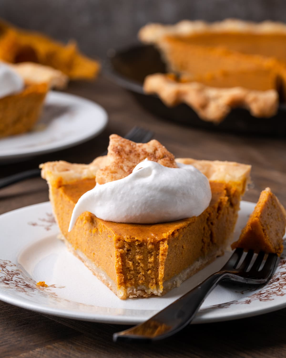 A slice of pumpkin pie on a plate topped with whipped cream and a sugar cookie, with a forkful of pie missing.