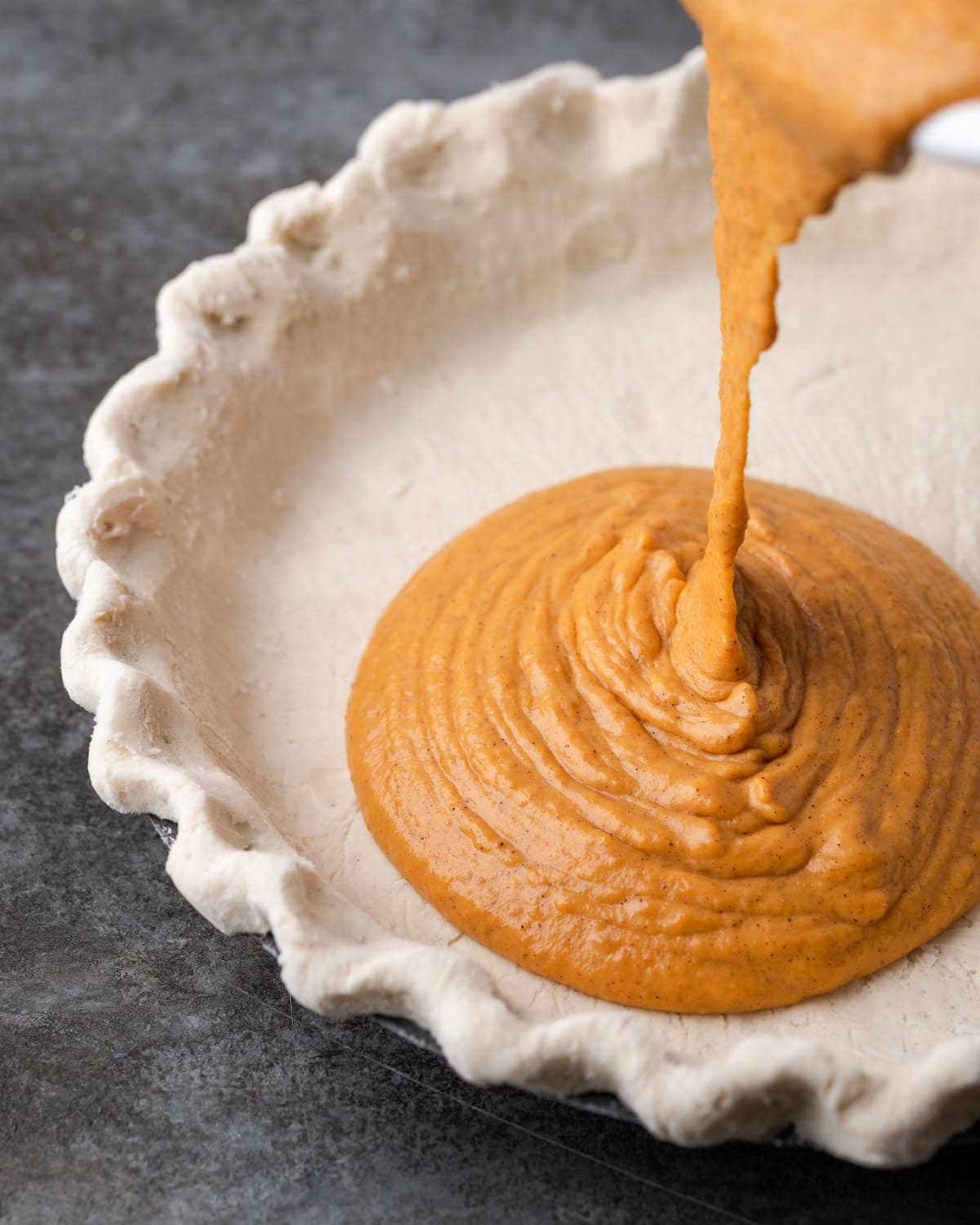 Pumpkin pie filling is poured into a pie crust.