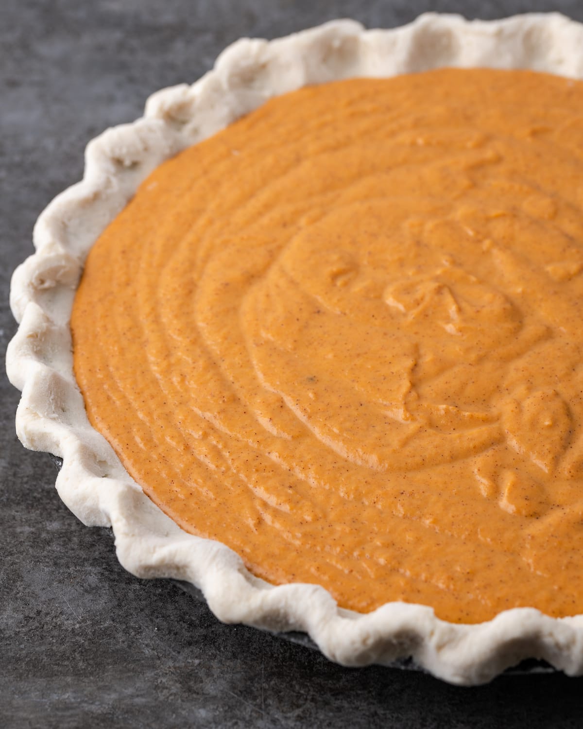 An unbaked pie crust filled with pumpkin pie filling.