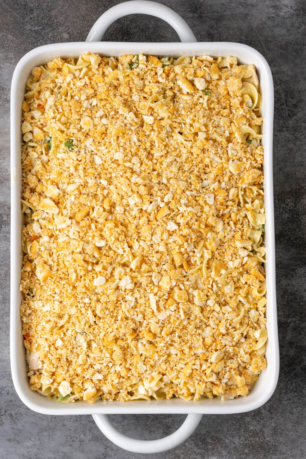 Overhead view of unbaked chicken noodle casserole in a baking dish topped with Ritz crackers.