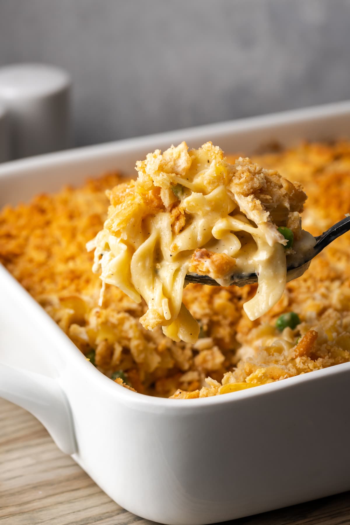 A scoop of chicken noodle casserole held over the rest of the casserole in a baking dish.
