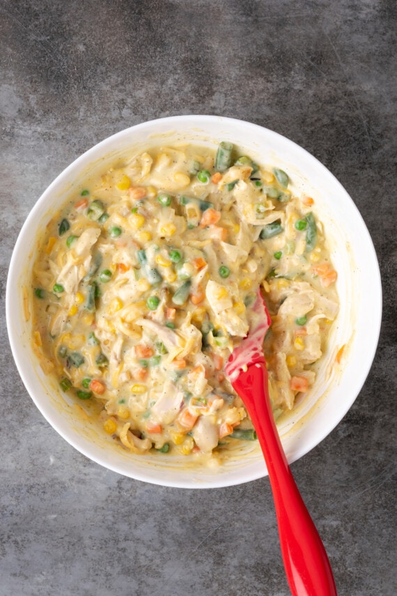 Creamy chicken casserole filling in a bowl with a red stirring spoon.