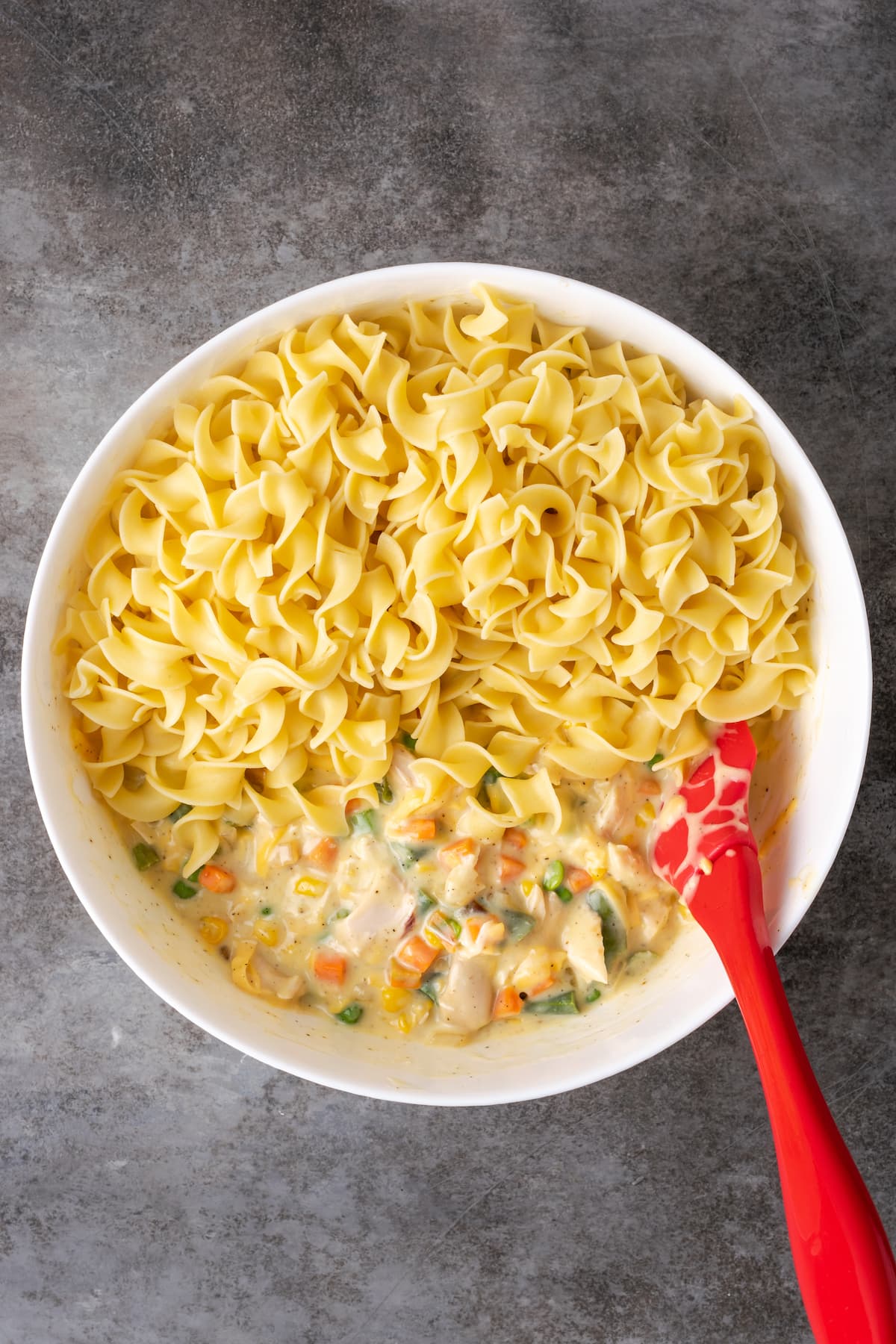 Egg noodles added to a bowl with creamy chicken noodle casserole filling.