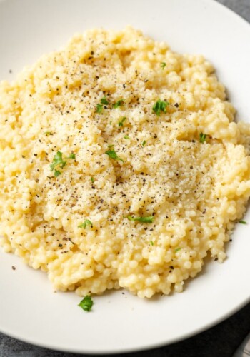 Overhead view of pastina served on a white plate topped with black pepper and parmesan.