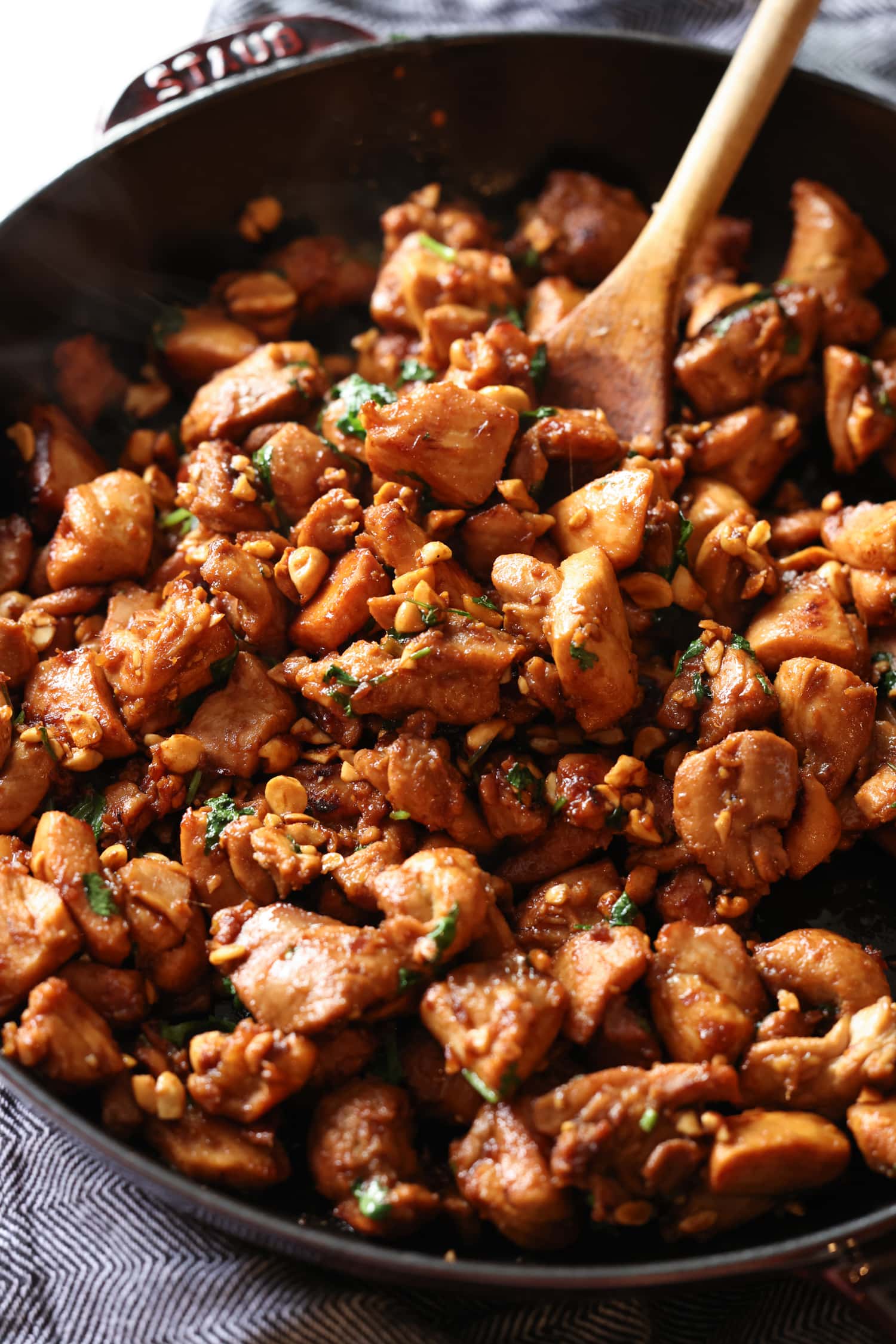 Ginger chicken is stirred with a wooden spoon while cooking in a cast iron skillet.