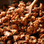 Ginger chicken is stirred with a wooden spoon while cooking in a cast iron skillet.