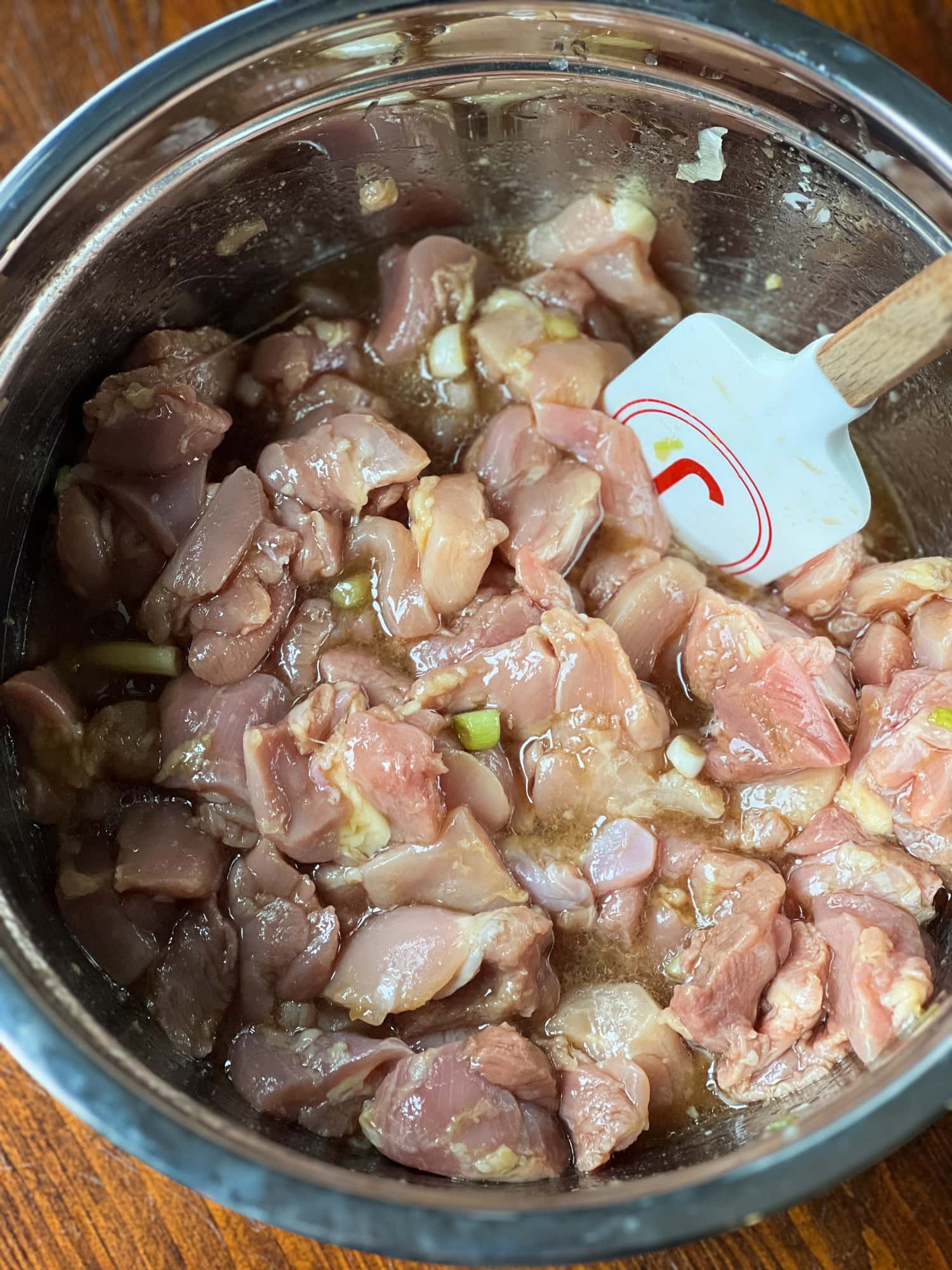 Uncooked chicken thigh pieces are mixed in a bowl of ginger and soy marinade.