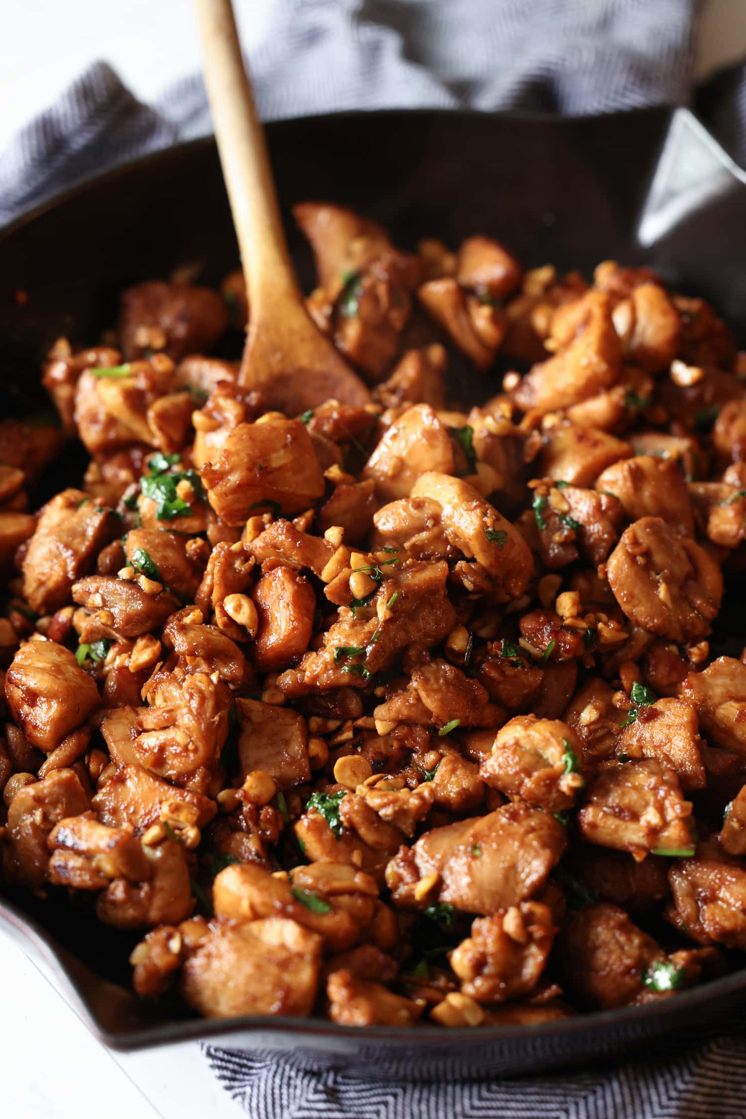 Ginger chicken is stirred with a wooden spoon as it cooks in a cast iron skillet.
