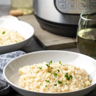 A bowl of creamy Instant Pot risotto garnished with fresh parsley, with the Instant Pot in the background.