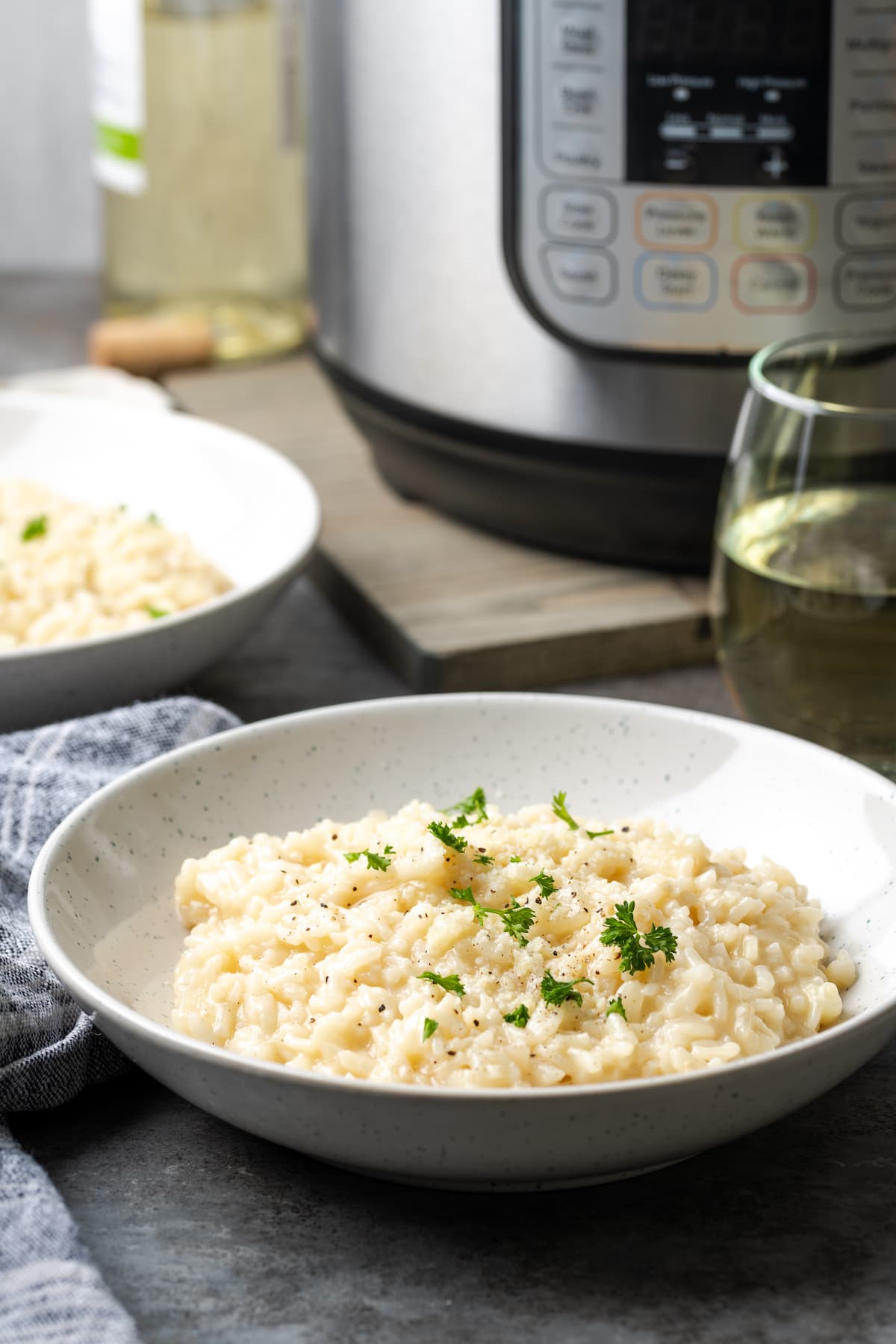 A bowl of creamy Instant Pot risotto garnished with fresh parsley, with the Instant Pot in the background.