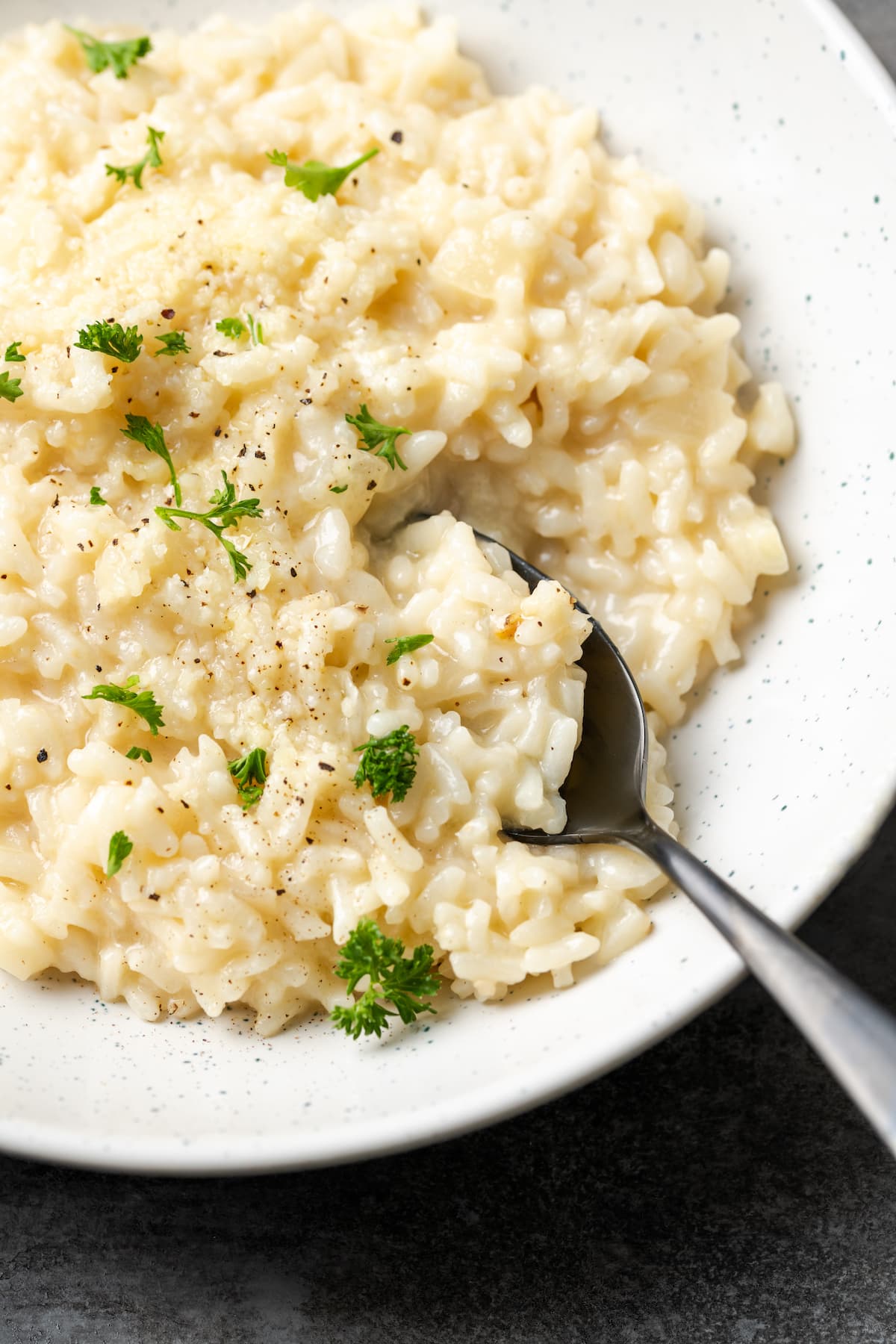 A bowl of creamy Instant Pot risotto with a spoon, garnished with fresh parsley.