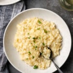 A bowl of creamy Instant Pot risotto with a spoon, garnished with fresh parsley.