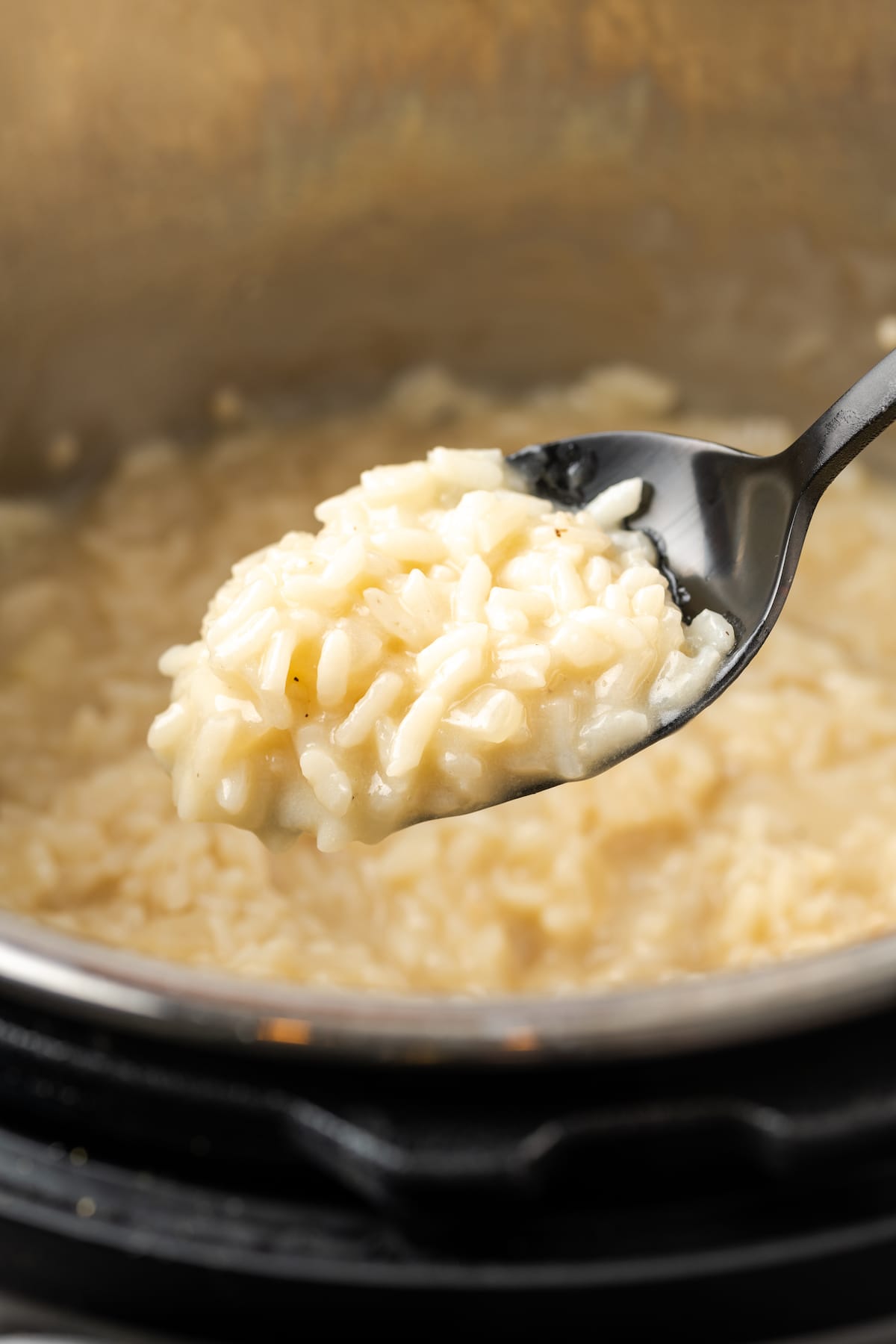 A spoonful of Instant Pot risotto with a pot full of risotto in the background.