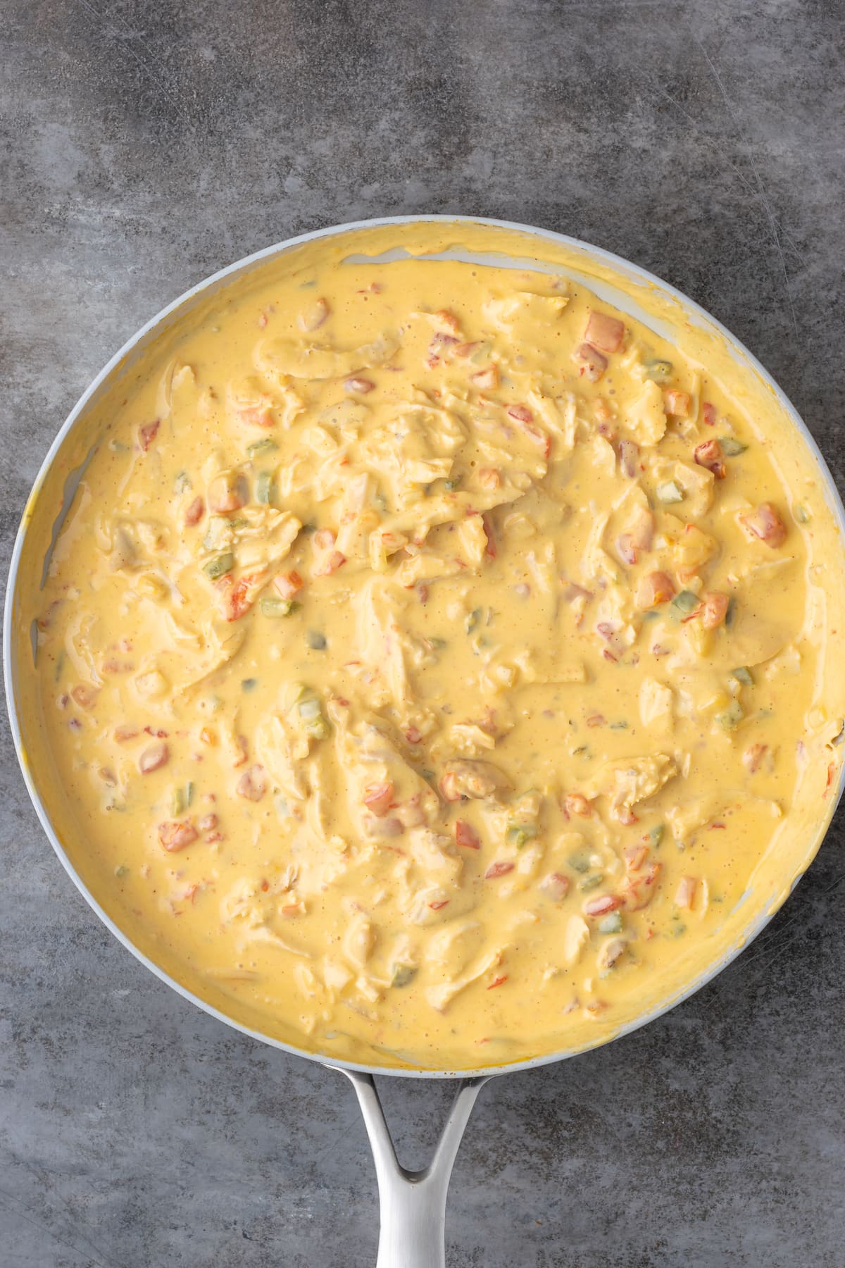 Mixing chicken into cheesy sauce in a skillet